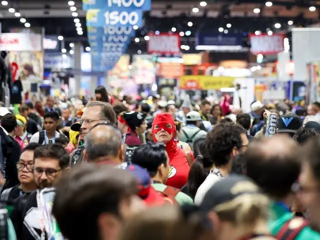 A cosplayer in a red superhero costume standing out in a packed convention crowd